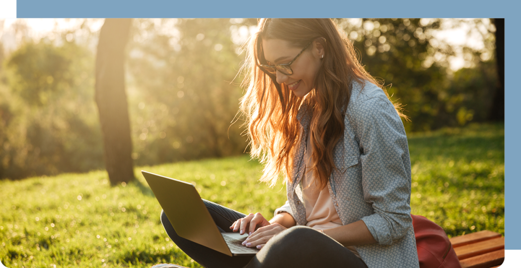 Image of young adult reading a laptop screen while sitting on grass.